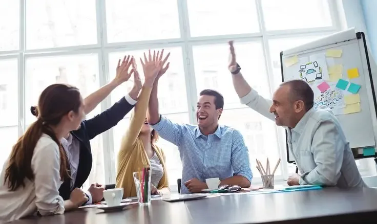 Happy team celebrating success in a modern office, highlighting improved teamwork and productivity through efficient back office outsourcing solutions.
